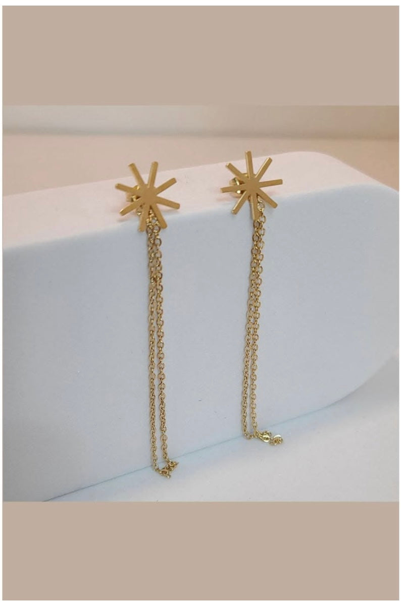 Gold star-shaped earrings with chain extensions on a white surface