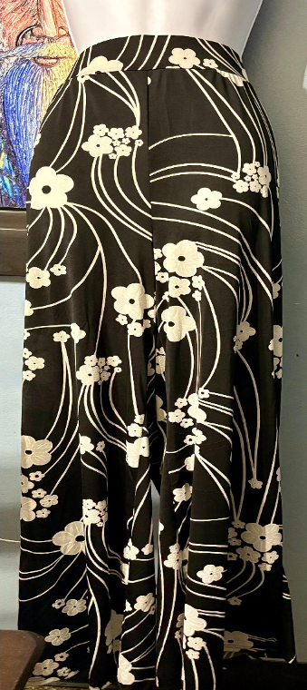 Black pants with white floral pattern on a mannequin against a neutral background
