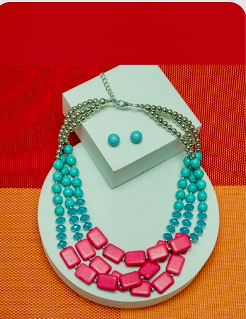 Necklace with pink and blue beads on a white stand against a red and orange checkered background