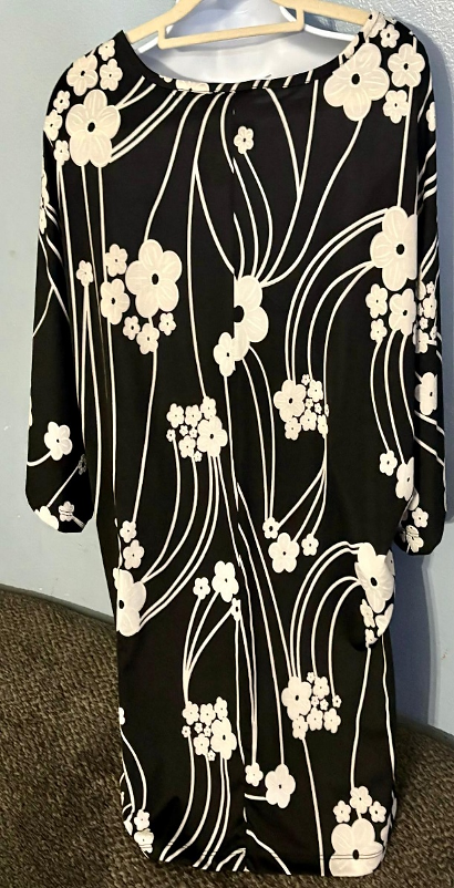 Black dress with white floral pattern on a hanger against a neutral background
